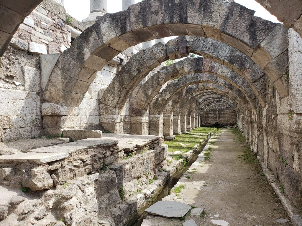 arches (no longer supporting a roof) continue into the distance, with a channel carved into the ground, lined with blocks