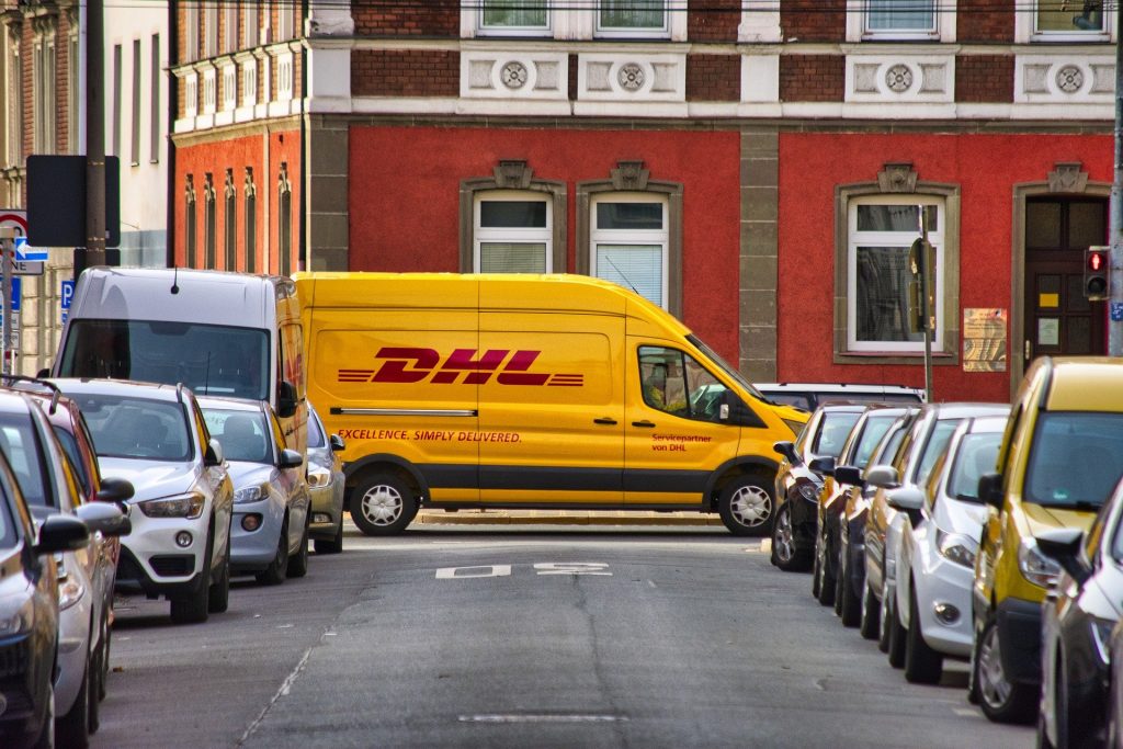 A yellow DHL delivery van drives along a residential street. Ethical travel shopping can reduce our carbon footprint.
