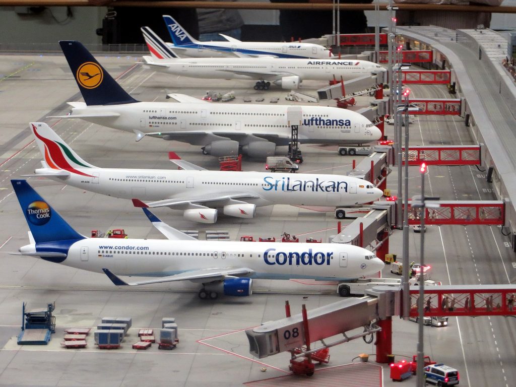 Large passenger aircraft sit at the gates as passengers board via air bridges. They are branded with the livery of Condor, Sri Lankan, Lufthansa, Air France and ANA. 