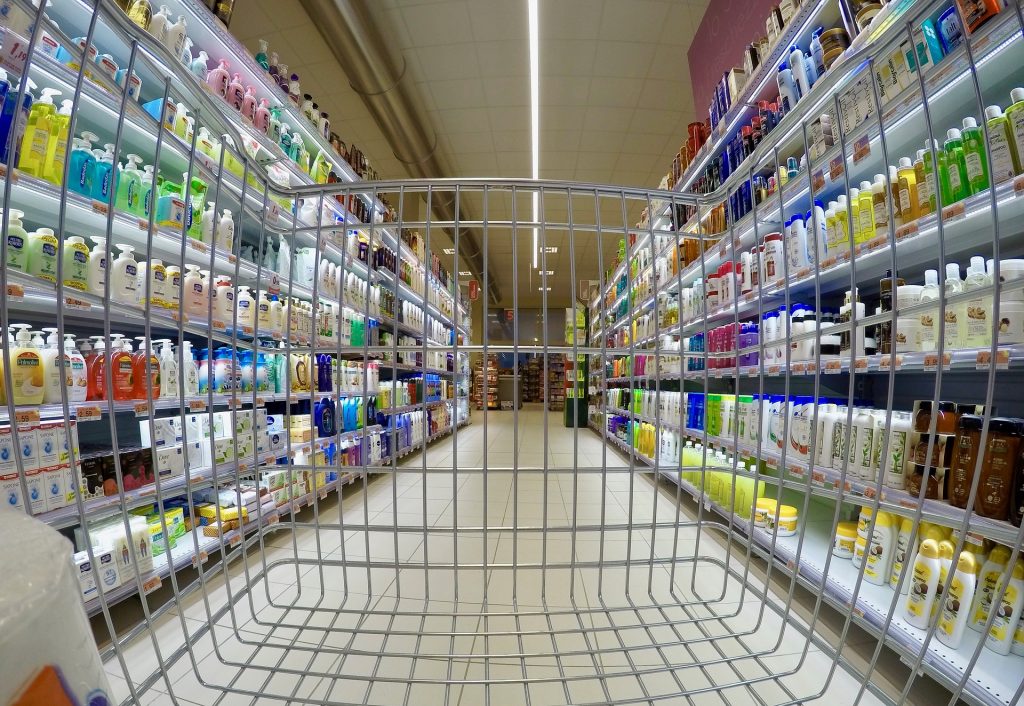 A wide-angle view of a supermarket aisle with toiletries: plastic bottles of hand soap, sunscreen, bars of soap, etc.