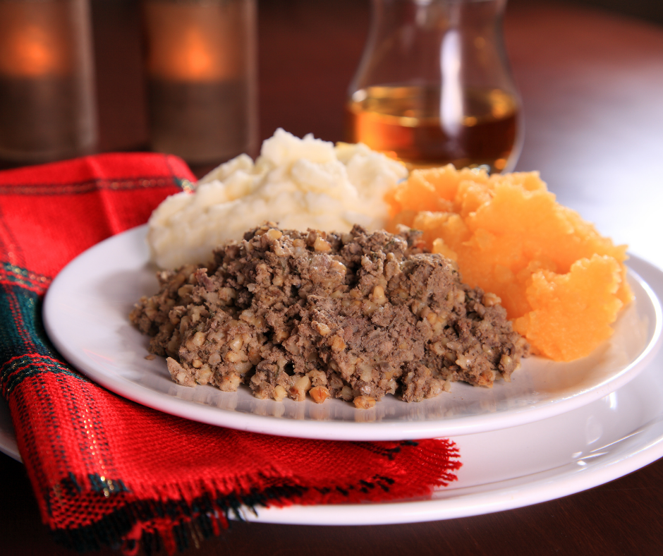 Haggis (a brown, ground meat) with mashed turnip and mashed potato on a plate, with a tartan napkin and a dram of whisky behind