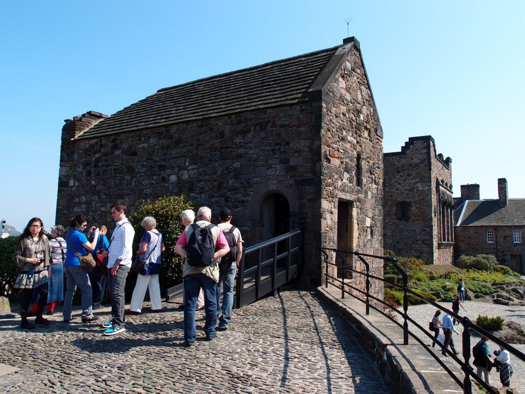 St Margaret's Chapel, a very old, dark stone building with a slate roof. A group of people nearby show that it is a similar size to the ten or so people with a doorway barely big enough for one person.